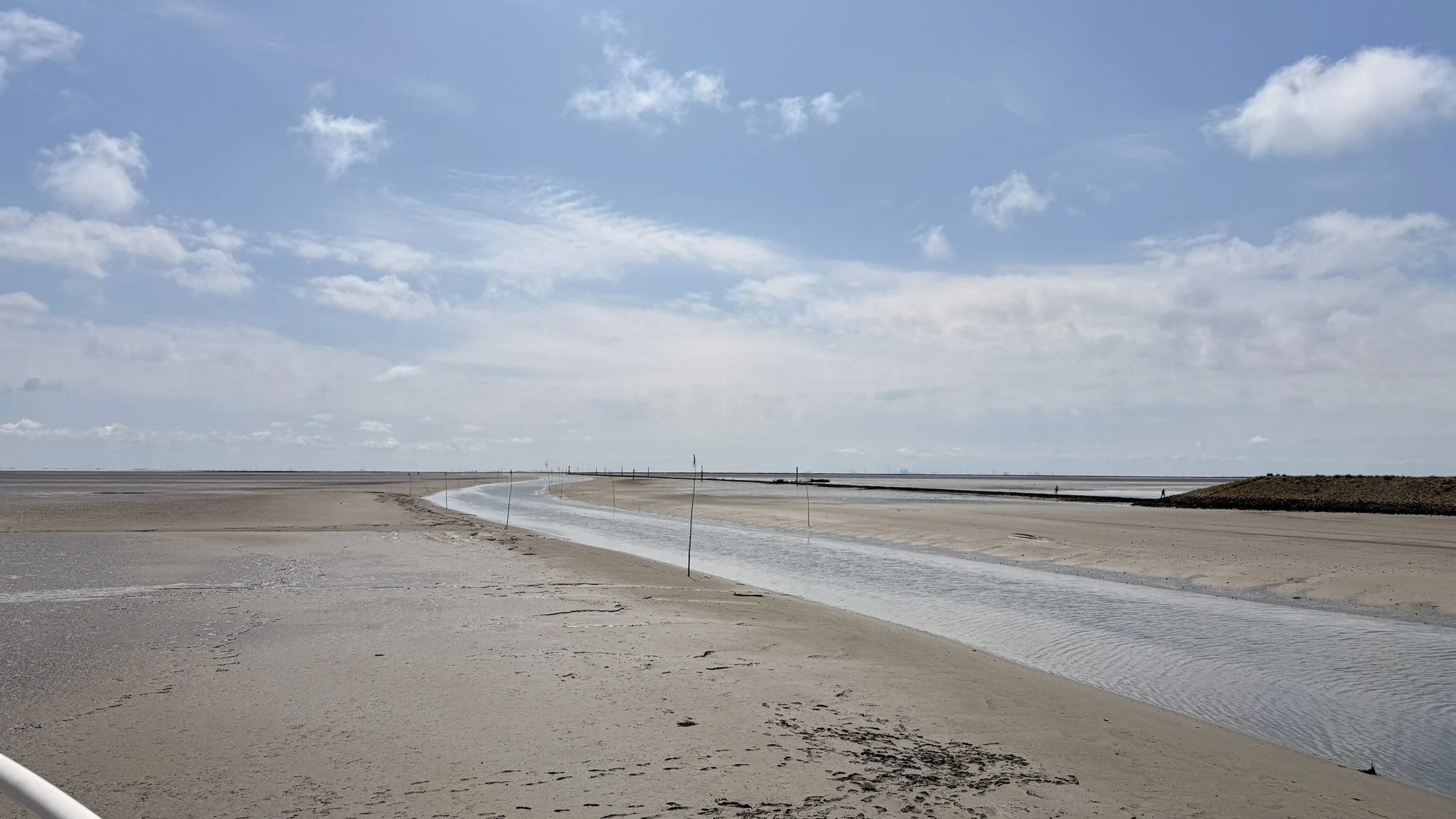 Geschwungener Priel im Watt unter blauem Himmel